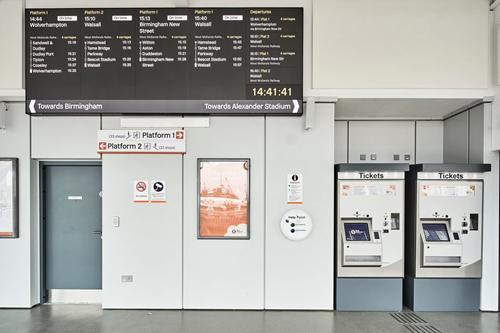Inside the Perry Barr railway station building, showing the customer information screen displaying the next trains and the ticket vending machines
